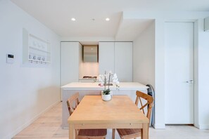 A modern kitchen with white cabinetry, a wooden dining table, and chairs. There is a small island with a sink and a vase of flowers. - StayAU High-Rise Luxury in CBD Apt @EQ Tower (Melbourne)
