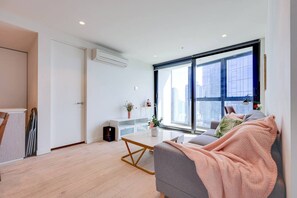 A modern living room with a sofa, a coffee table, and a large window offering a city view. - StayAU High-Rise Luxury in CBD Apt @EQ Tower (Melbourne)