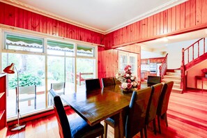 A dining area with a wooden table and chairs, a vase of flowers, and a view of the outdoors through large windows. - StayAU Spacious 2-Story Retreat & Easy City Access (Mont Albert North)