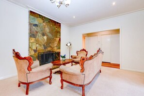 A room with a stone fireplace, a chandelier, and a dining area with a table and chairs. - StayAU Spacious 2-Story Retreat & Easy City Access (Mont Albert North)