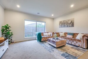A spacious living room with a large window, a sectional sofa, a coffee table, and a painting on the wall. - StayAU Luxury Double-Story Home | A/C Throughout (Clyde)