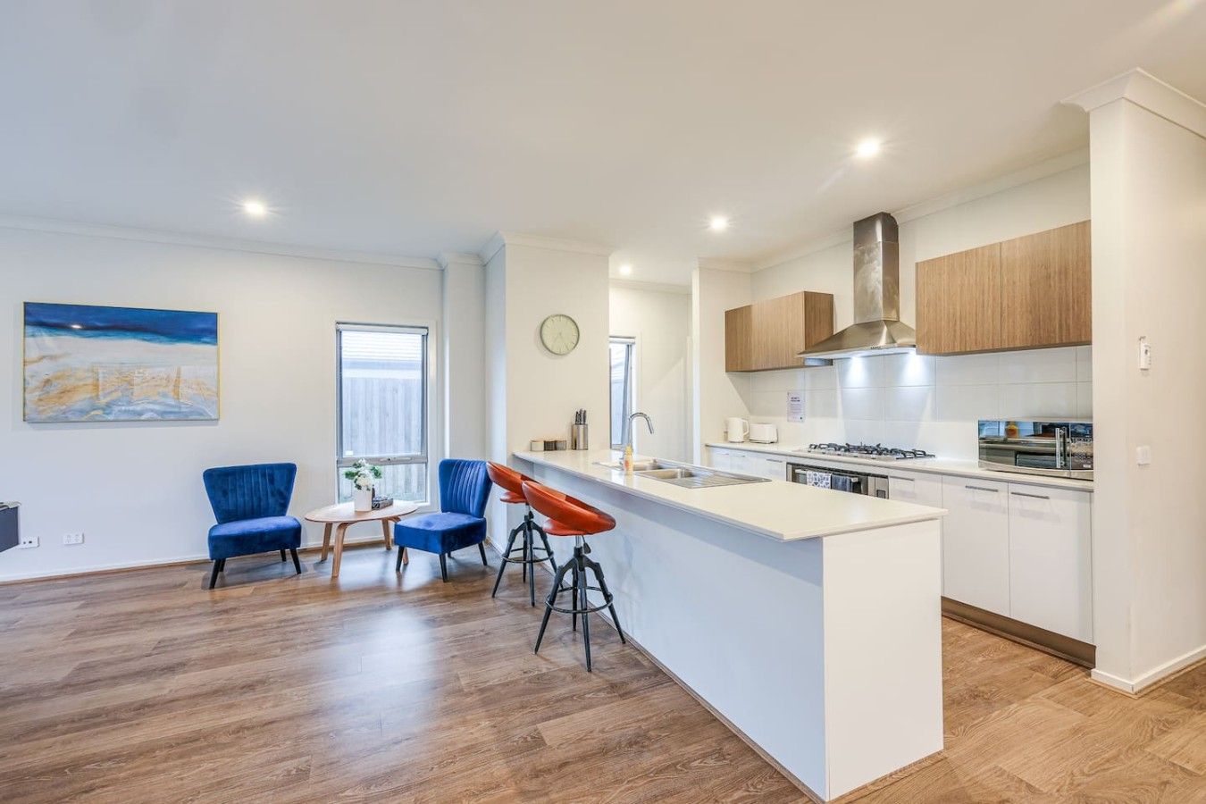 Una cocina moderna con una isla central, armarios de madera y un comedor con sillas azules.