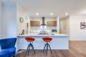 A modern kitchen with a central island, two bar stools, and a blue chair. - StayAU Luxury Double-Story Home | A/C Throughout (Clyde)