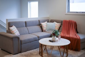 A living room with a grey sofa, a round coffee table, and a window with blinds. - StayAU Luxury Double-Story Home | A/C Throughout (Clyde)