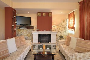 Ein Wohnzimmer mit Kamin aus Stein, zwei Sofas, einem Flachbildfernseher und einem Glastisch.