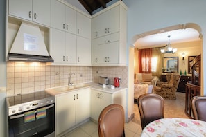 A kitchen with white cabinets, a stove, and a sink. There is a dining area with a table and chairs. - House in Kassiopi village, 400m from sea (Kassiopi)