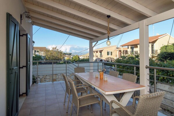 Eine überdachte Terrasse im Freien mit Tisch und Korbstühlen, mit Blick auf eine Wohngegend.
