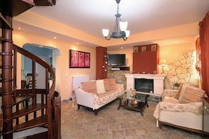 A living room with two sofas, a fireplace, a television, and a staircase. - House in Kassiopi village, 400m from sea (Kassiopi)