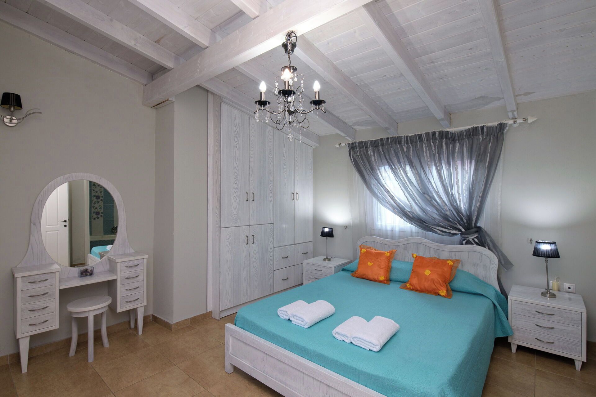 A bedroom with a bed, a dresser, a mirror, a wardrobe, and a chandelier.