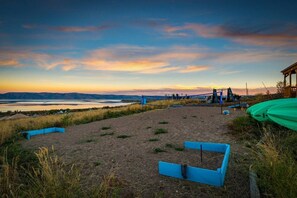 A beach with a clear view of the water, a blue seating area, and a green kayak. - Oso Blue - The Black Bear (Garden City)