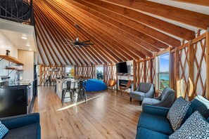 Un loft spazioso con soffitto alto, travi in legno, angolo pranzo, posti a sedere e televisione.