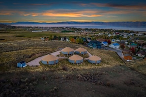 A rural landscape with yurts and houses, a clear sky, and a distant body of water. - Oso Blue - The Cisco | Yurt Experience! Outdoor Games, BBQ, Views, & More (Garden City)