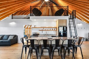 A spacious loft with a high ceiling, a kitchen with modern appliances, and a dining area with a large table and chairs.