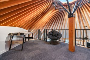 A modern interior with a sloped ceiling, a workbench, a cushioned chair, and a metal railing. - Oso Blue - The Rendezvous | Yurt Experience! Outdoor Games, BBQ, Views, & More (Garden City)