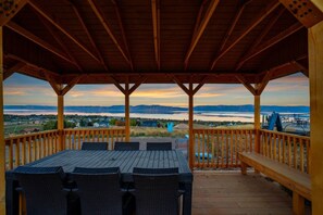 A covered outdoor seating area with a view of a lake and mountains. - Oso Blue - The Rendezvous | Yurt Experience! Outdoor Games, BBQ, Views, & More (Garden City)