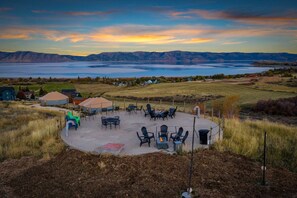 A patio area with outdoor furniture, a covered seating area, and a view of a lake and distant mountains. - Oso Blue | 5 Yurt Compound! Sleeps 60! Lawn Games! BBQs! (Garden City)