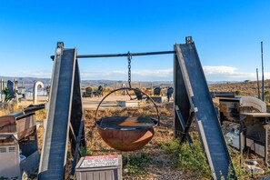 A rustic outdoor area with a large metal pot suspended by chains, surrounded by metal structures and a clear sky. - Oso Blue | 5 Yurt Compound! Sleeps 60! Lawn Games! BBQs! (Garden City)