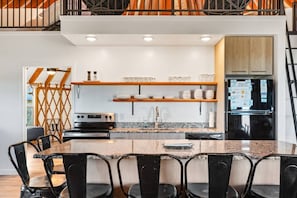 A modern kitchen with a granite countertop, stainless steel appliances, and wooden shelves.