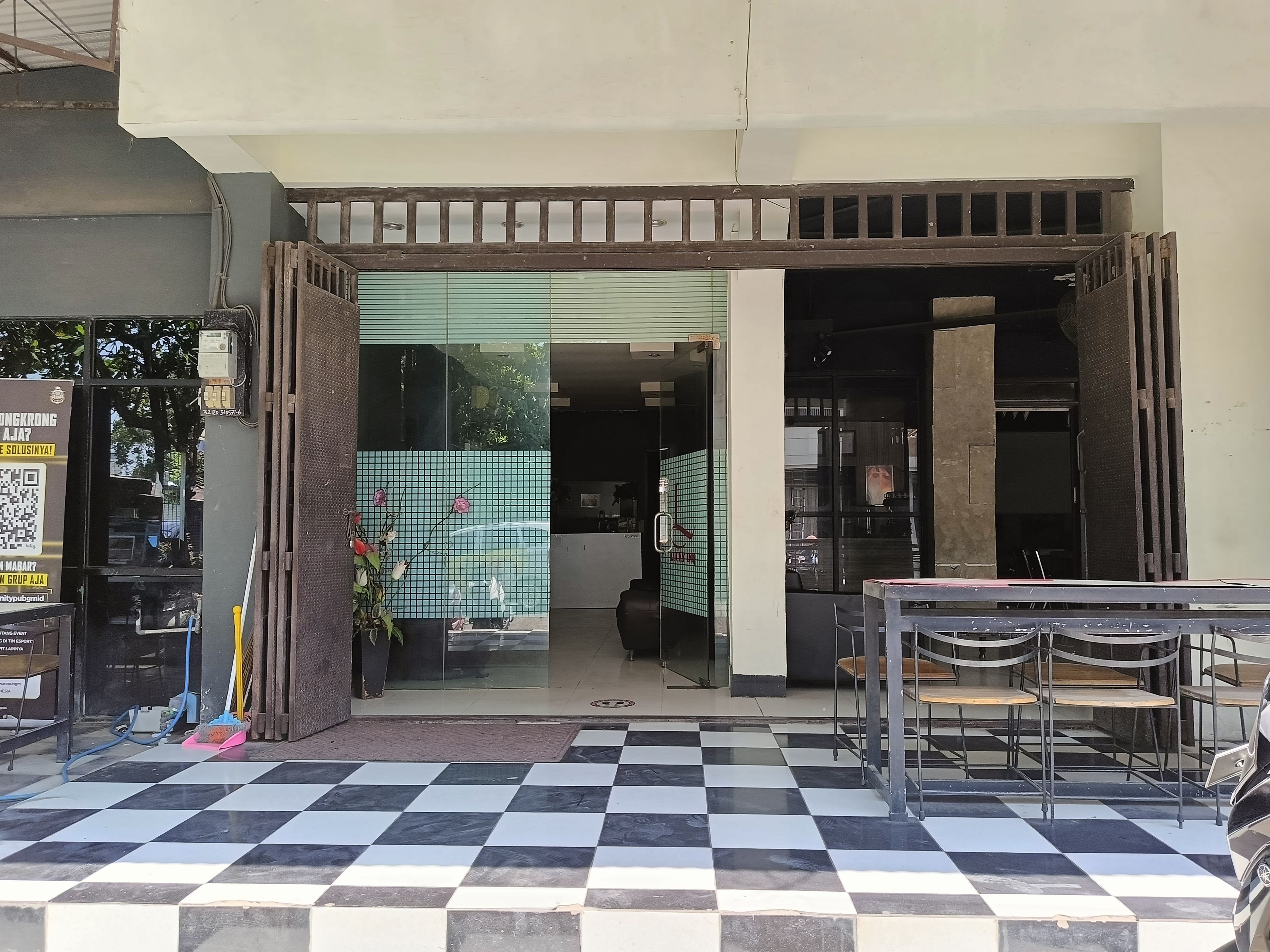 A cafe with a checkered floor, a counter with chairs, and a glass door leading inside.
