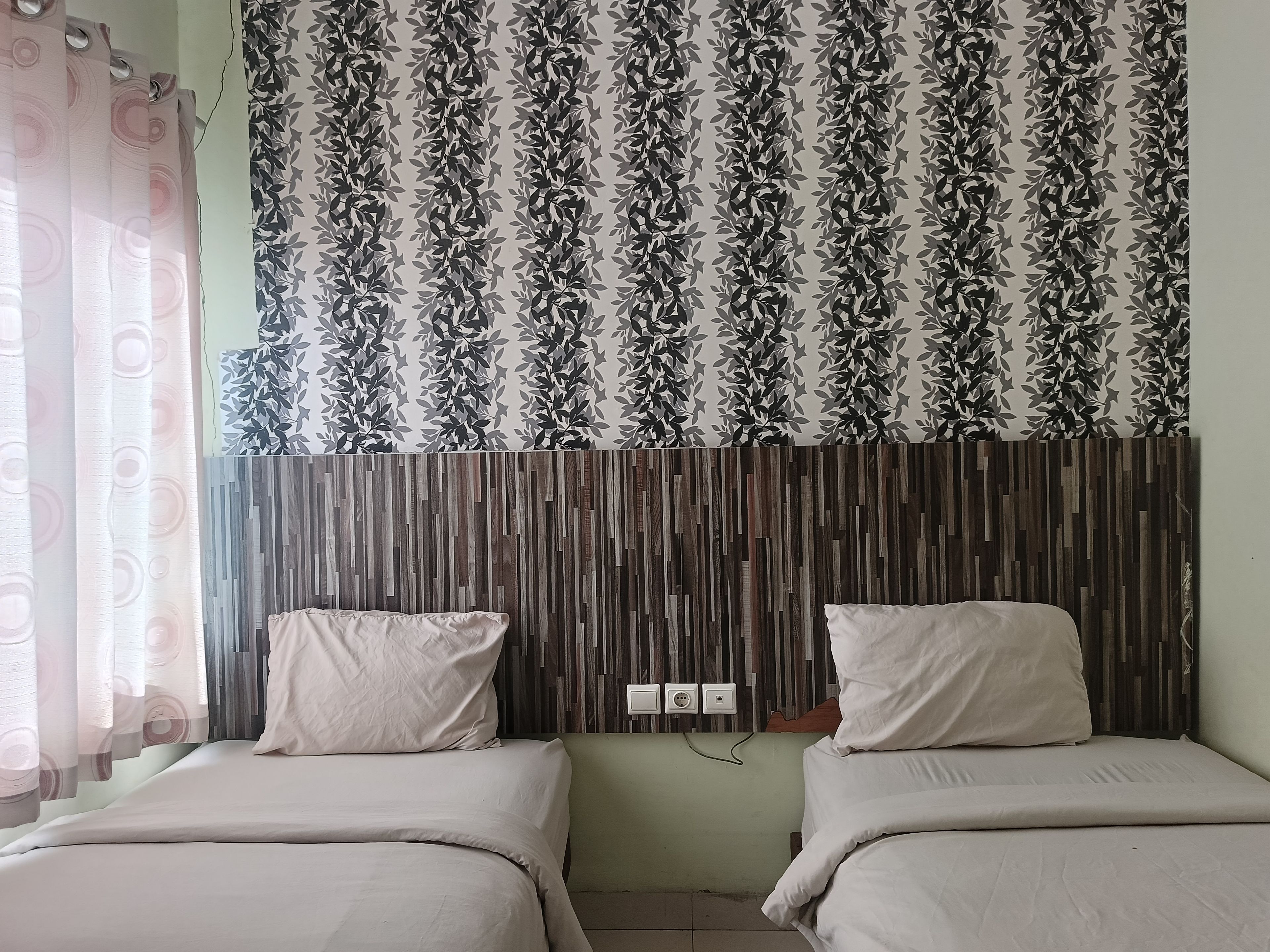 A room with two beds, a patterned curtain, and a wooden headboard.