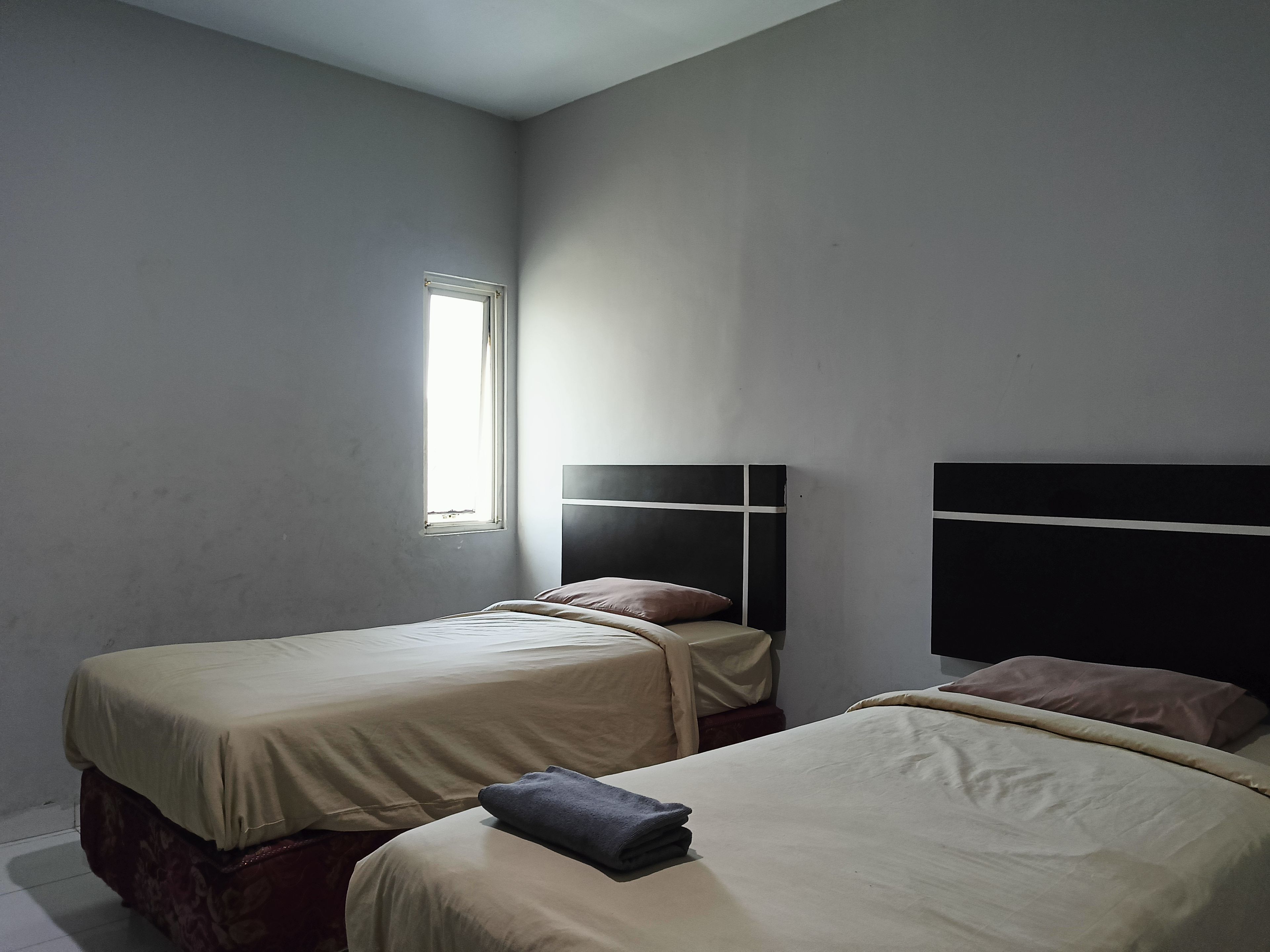 A room with two beds, each with a headboard, a window, and a plain wall.