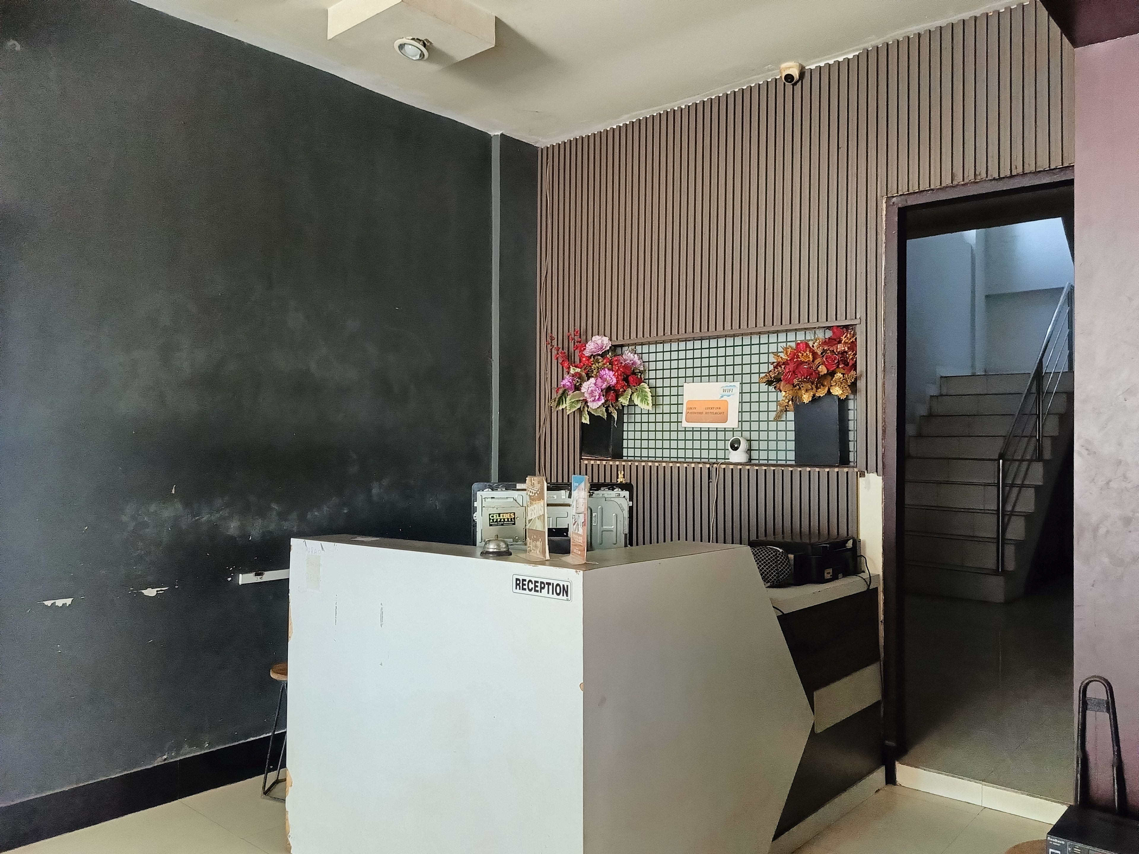 A reception area with a reception desk, a security camera, a sign indicating WiFi availability, and a staircase leading to an upper floor.