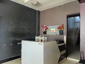 A reception area with a reception desk, a security camera, a sign indicating WiFi availability, and a staircase leading to an upper floor. - Hotel O near Mall Panakkukang (Makassar)