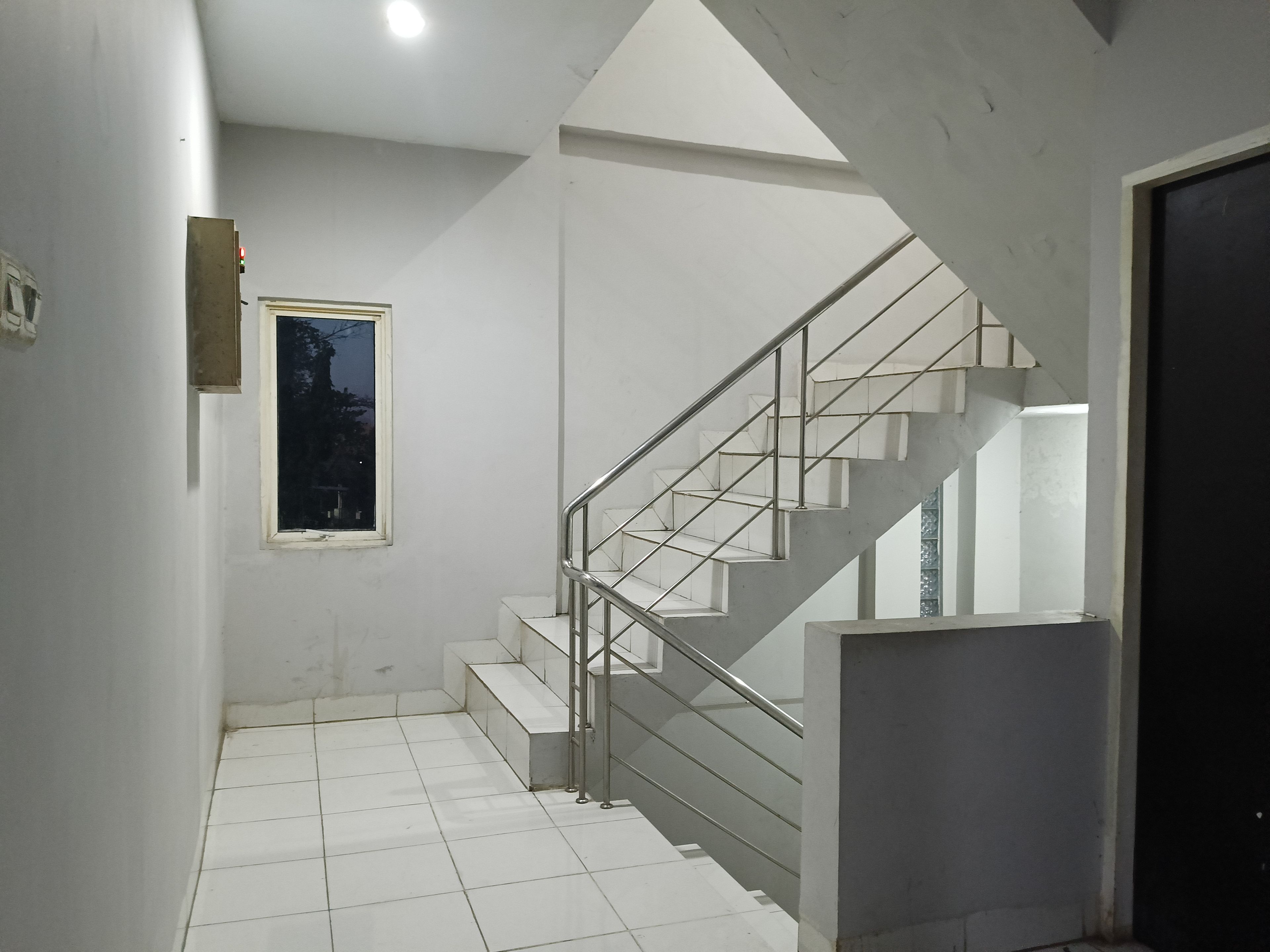 A staircase with metal railings leading to an upper floor, a window with a view of trees, and a tiled floor.