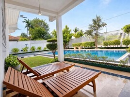 A poolside area with wooden lounge chairs, a clear view of the pool, and a white fence in the background.