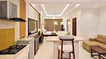A modern hotel room with a kitchenette, a dining area, a sofa, and a bar area.