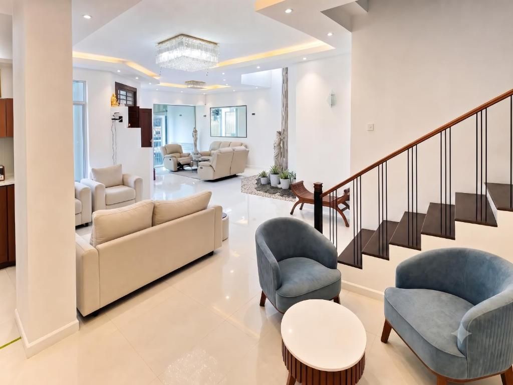 Una sala de estar moderna con un sofá, dos sillones, una mesa de centro redonda y una escalera con barandilla de madera.