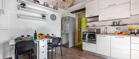 Una cocina moderna con armarios blancos, un refrigerador de acero inoxidable y un comedor con dos sillas y una mesa para dos.