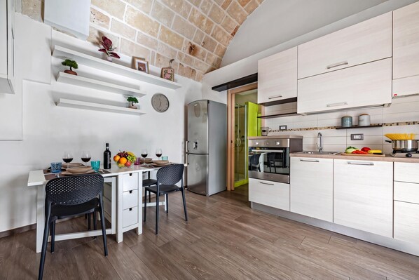 A modern kitchen with white cabinetry, a stainless steel refrigerator, and a dining area with two chairs and a table set for two.