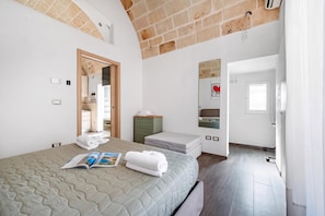 A bedroom with a bed, a bedside table, a mirror, and a door leading to another room.