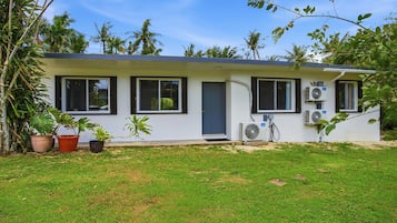 A single-story house with a flat roof, a front door, and two windows on the ground floor. There are two air conditioning units mounted on the exterior wall.