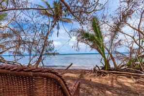 Una silla de mimbre con vista a una playa con palmeras y una vista despejada del océano.