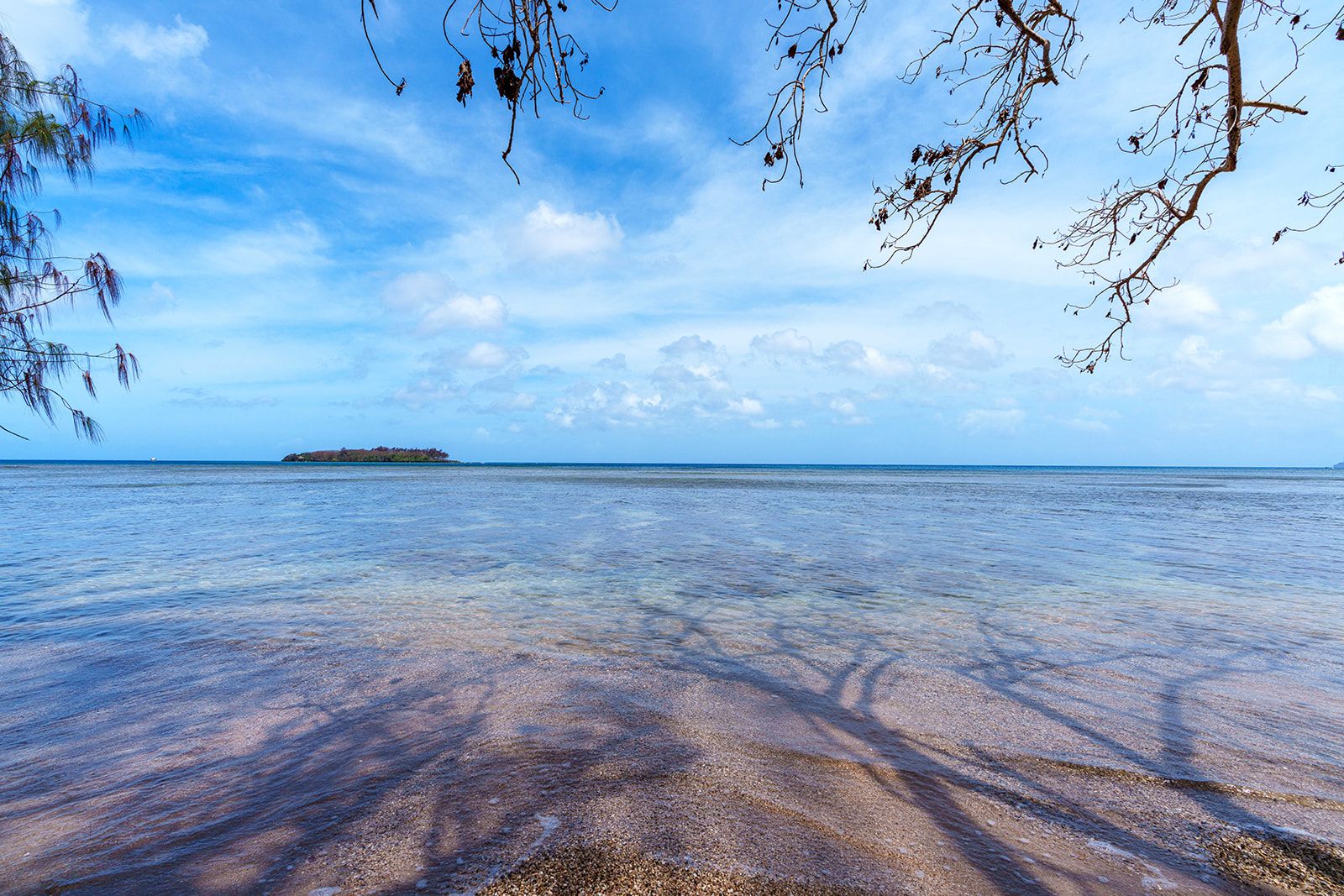 Ein Strand mit klarem Wasser, einer entfernten Insel und wolkenlosem Himmel.