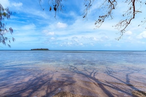 A beach with clear water, a distant island, and a clear sky.