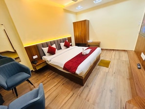 A hotel room with a bed, two nightstands, a wardrobe, and a seating area with chairs. - Hotel Shiv Sadhana (Varanasi)