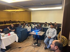 A conference room with a projector, a table with a laptop, and attendees seated. - Hotel Shiv Sadhana (Varanasi)