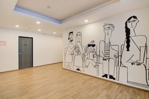 A spacious room with a wooden floor, a grey door, and a wall mural depicting cartoon characters. - Townhouse The AMV Hotel (Gurugram)