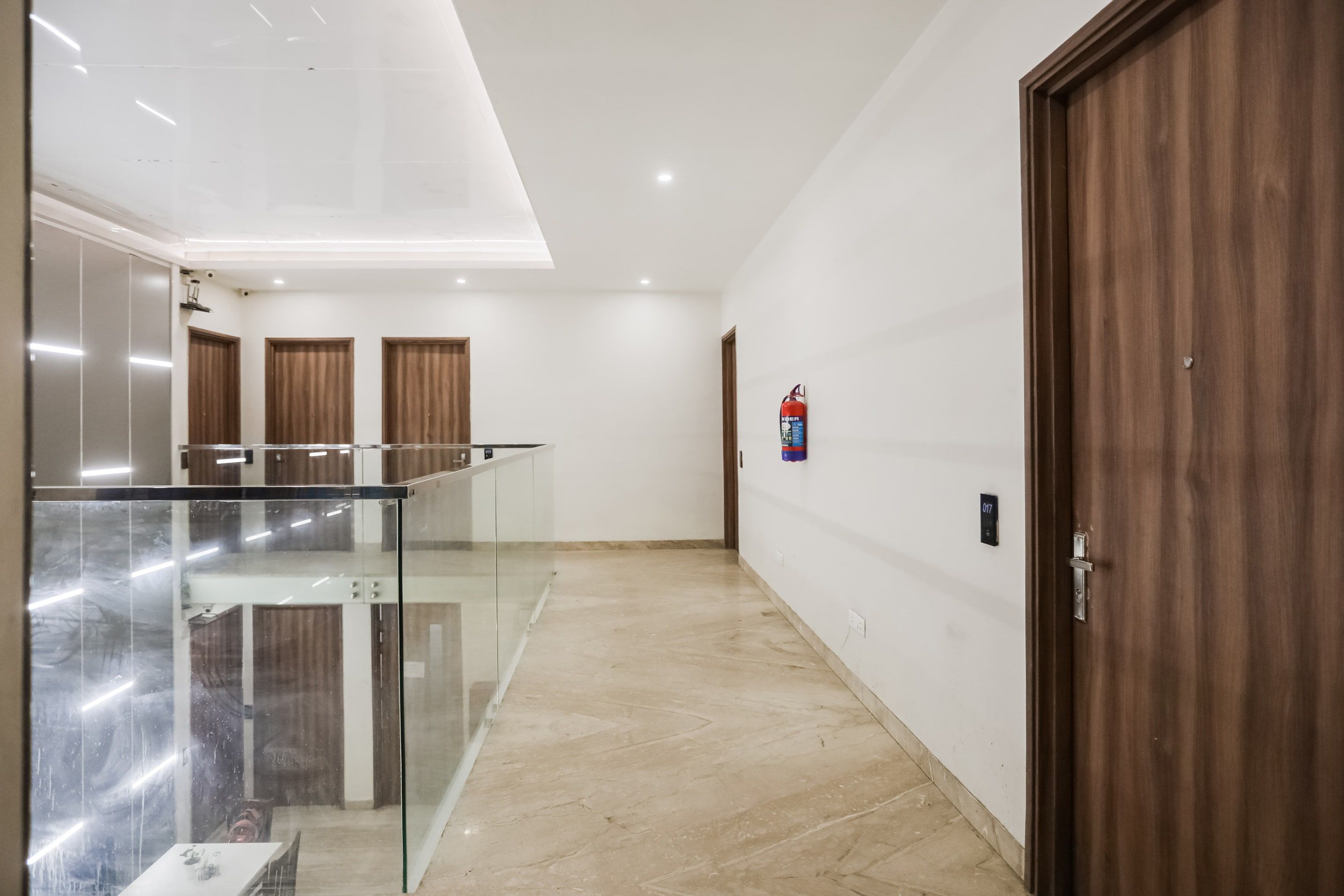 A hotel corridor with a glass railing, wooden doors, and a fire extinguisher on the wall.