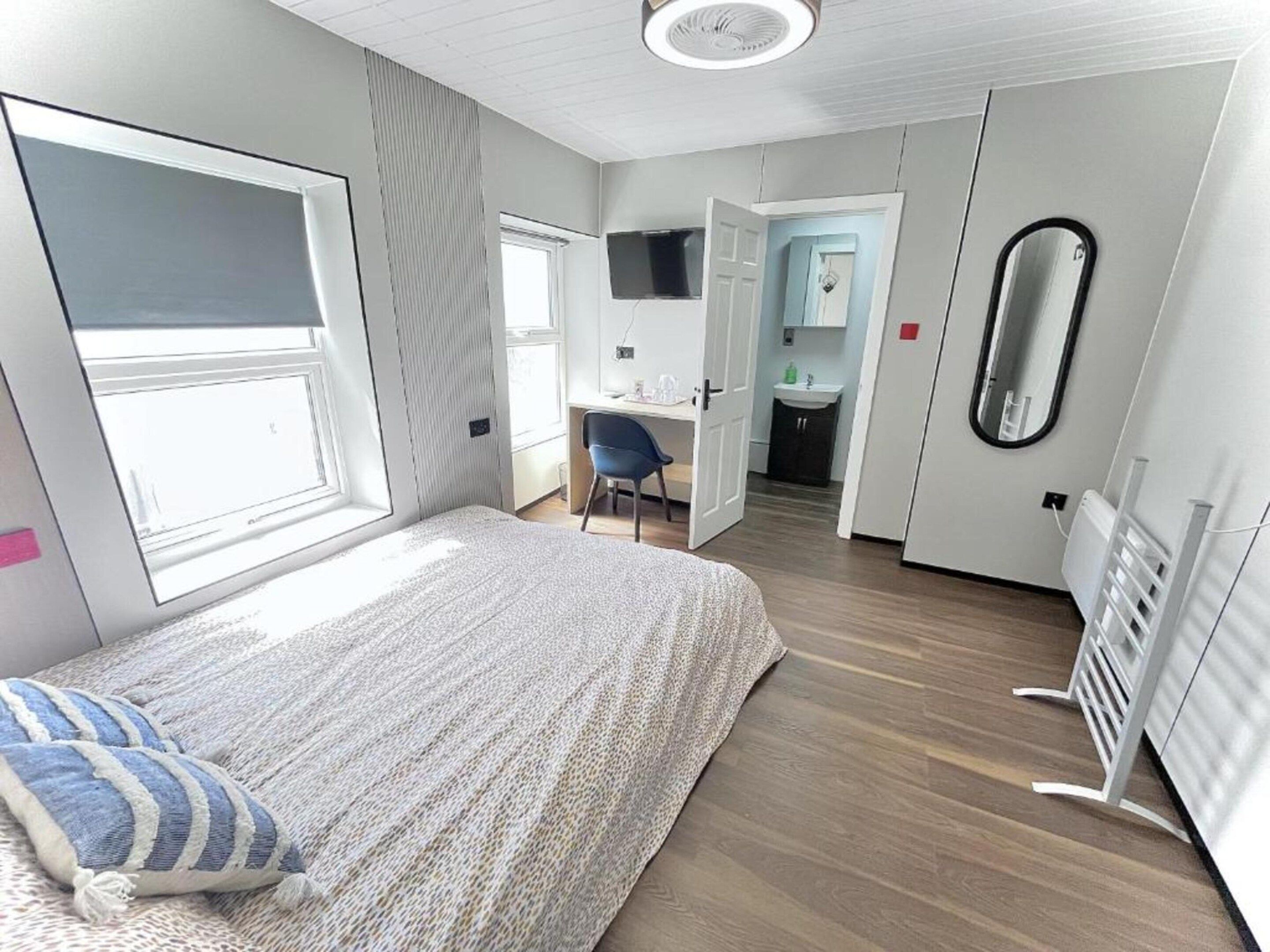 A modern bedroom with a large bed, a desk, and a bathroom in the background.