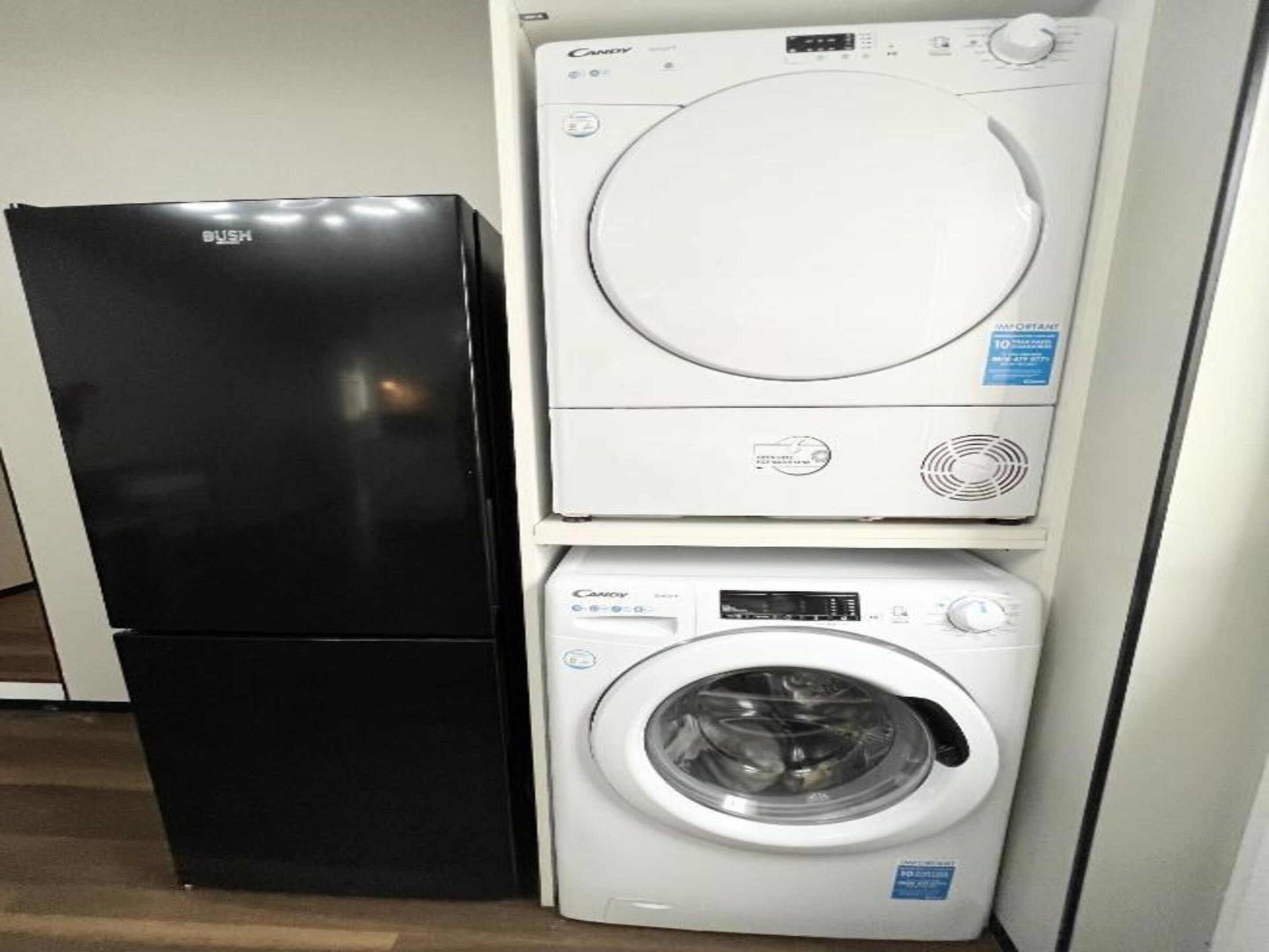 A black refrigerator and a stacked washer and dryer unit.