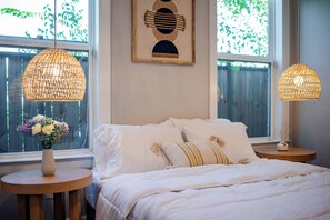 A bedroom with a bed, two bedside tables, a vase with flowers, and a wall-mounted artwork. - Designer Home w/ Garage, Fenced Yard & Patio (Houston)