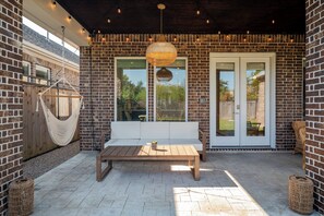 A covered patio with a wooden bench, a hanging light fixture, and a brick wall. - Designer Home w/ Garage, Fenced Yard & Patio (Houston)