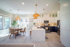 A modern kitchen with white cabinetry, a marble island, and pendant lighting. - Designer Home w/ Garage, Fenced Yard & Patio (Houston)