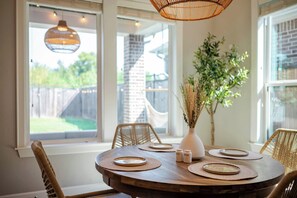 A dining area with a round table set for four, surrounded by wicker chairs, a vase with dried plants, and salt and pepper shakers. - Designer Home w/ Garage, Fenced Yard & Patio (Houston)