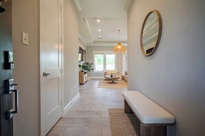 A hallway with a bench, a door, a mirror, and a hanging light fixture. - Designer Home w/ Garage, Fenced Yard & Patio (Houston)