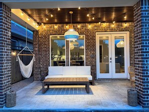 An outdoor seating area with a bench, a hanging hammock, and a dining table. - Designer Home w/ Garage, Fenced Yard & Patio (Houston)